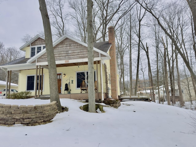 snow covered house featuring a porch and a chimney