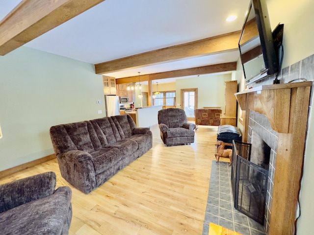 living room featuring baseboards, a tile fireplace, beamed ceiling, light wood-type flooring, and a notable chandelier