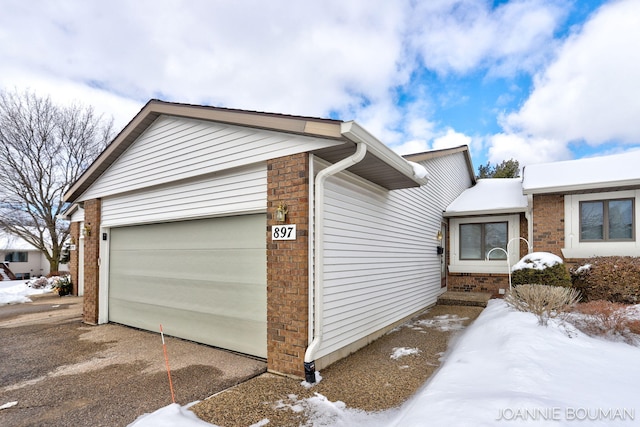 snow covered property featuring a garage and brick siding