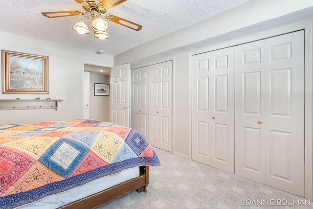 carpeted bedroom featuring a textured ceiling, two closets, and a ceiling fan