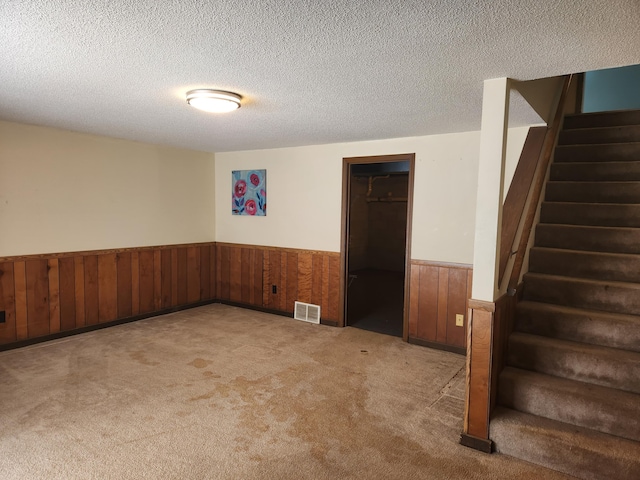 carpeted empty room with a textured ceiling, stairway, wainscoting, and visible vents