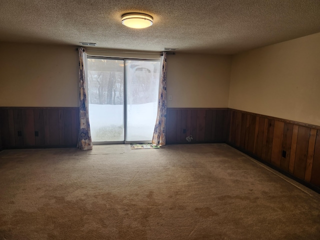 carpeted spare room with a wainscoted wall, wood walls, and a textured ceiling