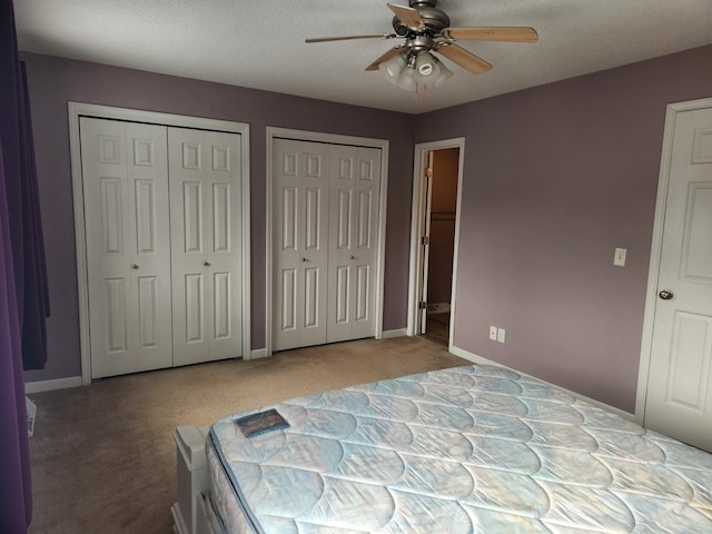 carpeted bedroom with ceiling fan, a textured ceiling, baseboards, and two closets