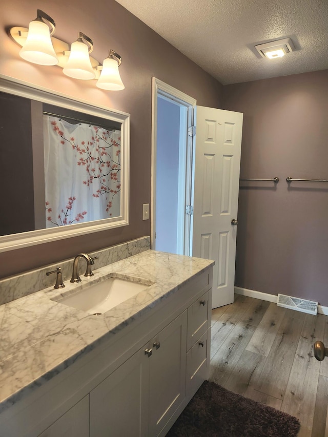 bathroom featuring baseboards, visible vents, wood finished floors, a textured ceiling, and vanity