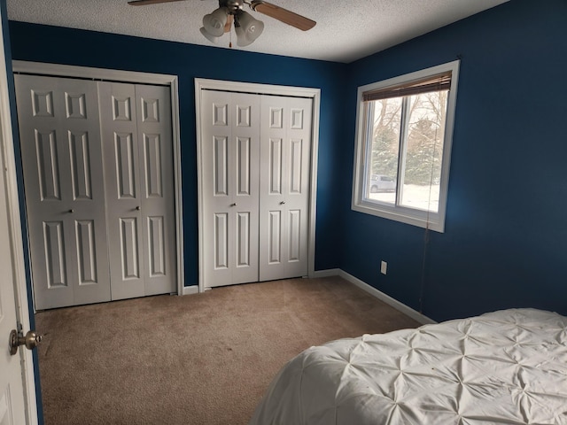 carpeted bedroom with a textured ceiling, baseboards, a ceiling fan, and multiple closets