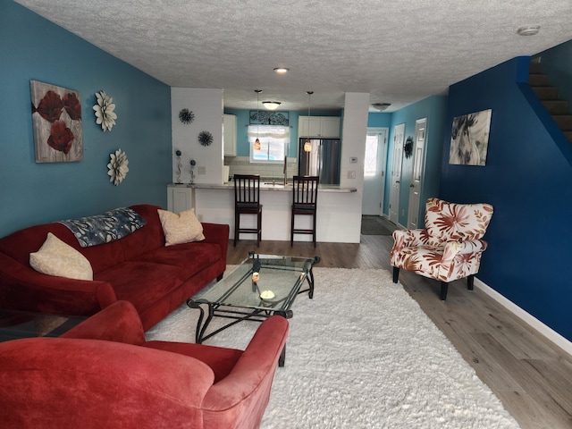 living room featuring a textured ceiling, stairway, wood finished floors, and baseboards