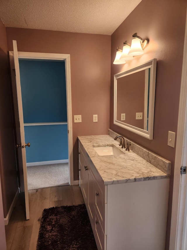 bathroom with a textured ceiling, wood finished floors, vanity, and baseboards