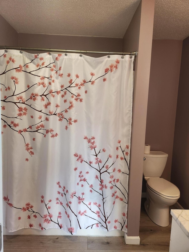 full bathroom featuring a textured ceiling, toilet, and wood finished floors