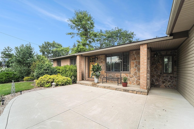 view of exterior entry with stone siding, brick siding, and a patio