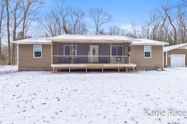 snow covered back of property with a sunroom, a detached garage, and an outdoor structure