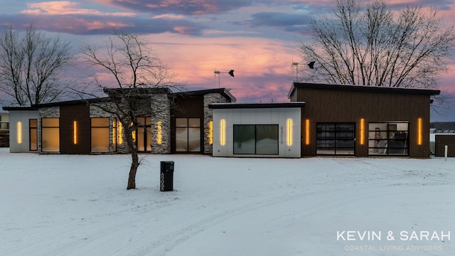 snow covered house with a garage and stone siding