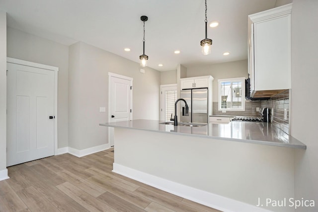 kitchen with white cabinetry, light countertops, decorative backsplash, stainless steel fridge, and pendant lighting