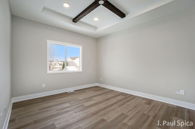 empty room with light wood finished floors, beamed ceiling, coffered ceiling, and baseboards