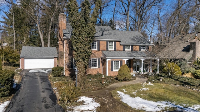 colonial-style house featuring an outbuilding, brick siding, a detached garage, roof with shingles, and a chimney