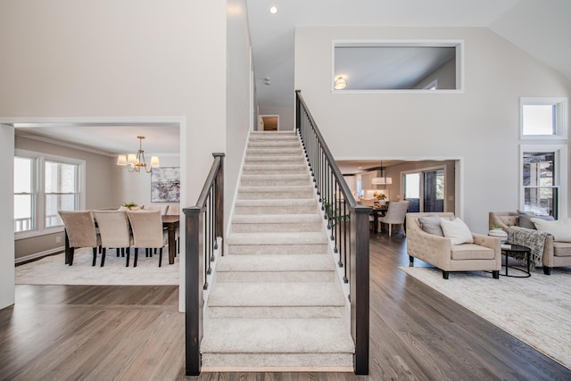 stairway with high vaulted ceiling, wood finished floors, and an inviting chandelier