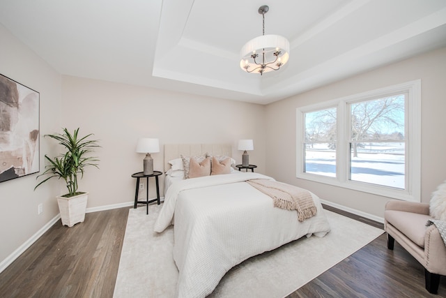 bedroom with dark wood-type flooring, a raised ceiling, a chandelier, and baseboards