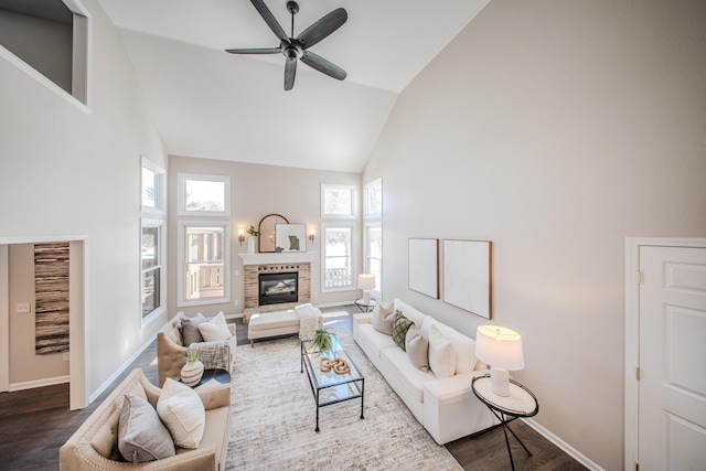 living room featuring ceiling fan, high vaulted ceiling, dark wood-style flooring, baseboards, and a brick fireplace