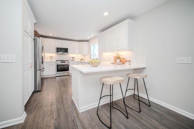 kitchen with a kitchen breakfast bar, a peninsula, stainless steel appliances, light countertops, and white cabinetry