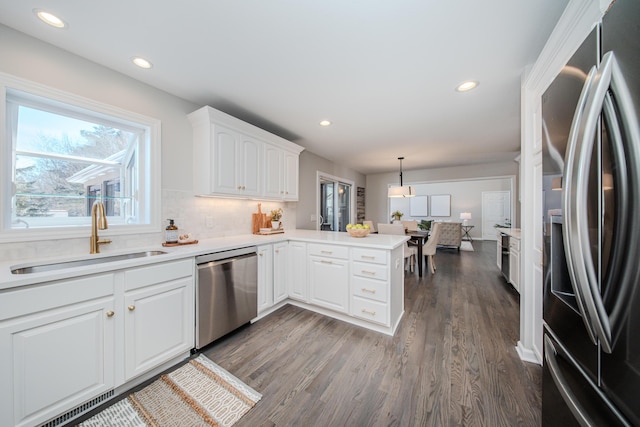 kitchen featuring appliances with stainless steel finishes, a peninsula, hanging light fixtures, light countertops, and a sink