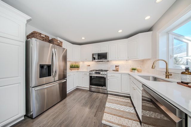 kitchen featuring light countertops, appliances with stainless steel finishes, white cabinetry, a sink, and wood finished floors