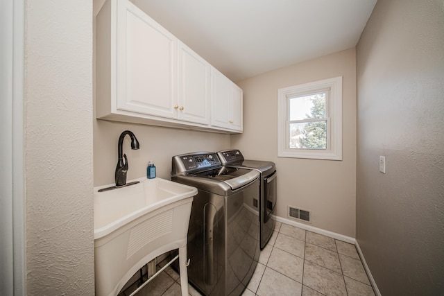 laundry area with light tile patterned floors, visible vents, baseboards, cabinet space, and washing machine and clothes dryer