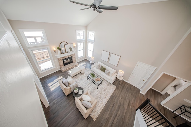 living area featuring dark wood-type flooring, a ceiling fan, a brick fireplace, high vaulted ceiling, and baseboards