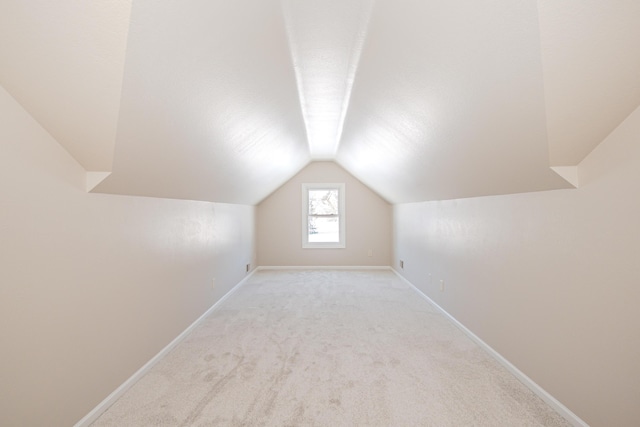 additional living space with light carpet, vaulted ceiling, and baseboards