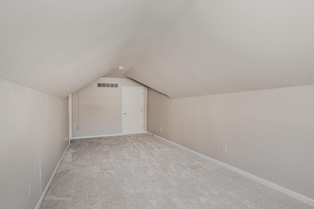 additional living space featuring visible vents, light carpet, vaulted ceiling, a textured ceiling, and baseboards