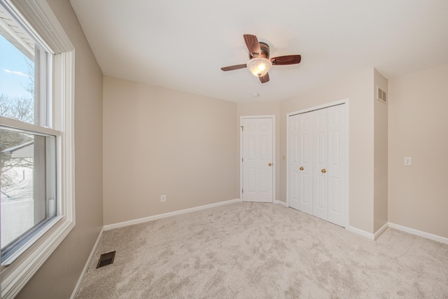 unfurnished bedroom featuring visible vents, baseboards, a ceiling fan, light colored carpet, and a closet