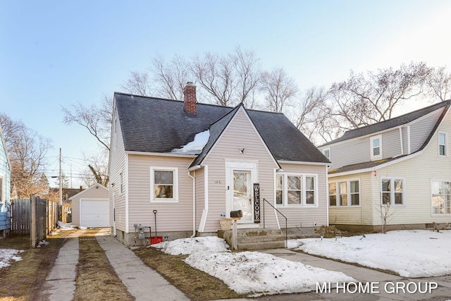 view of front of property with driveway, a detached garage, a chimney, roof with shingles, and an outbuilding