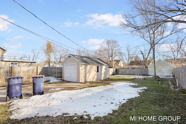 yard covered in snow featuring a fenced backyard, a detached garage, and an outbuilding