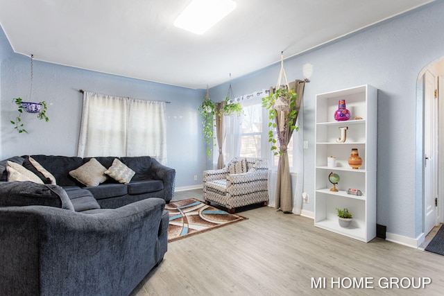 living room with arched walkways, baseboards, and wood finished floors