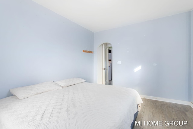 bedroom featuring light wood-style floors, baseboards, and arched walkways