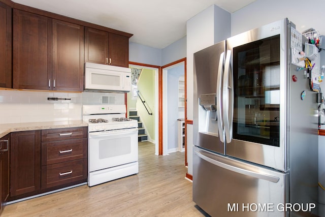 kitchen with light stone counters, light wood-style flooring, white appliances, dark brown cabinets, and backsplash