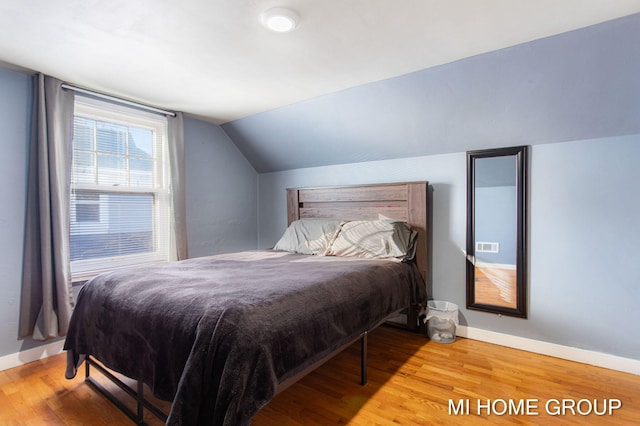 bedroom with light wood-style flooring, baseboards, and vaulted ceiling