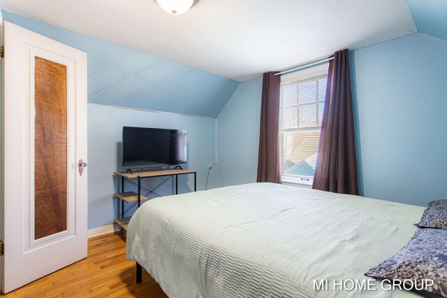 bedroom with light wood-style floors, baseboards, and vaulted ceiling