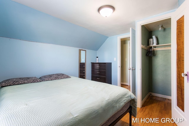 bedroom with vaulted ceiling, a closet, wood finished floors, and baseboards