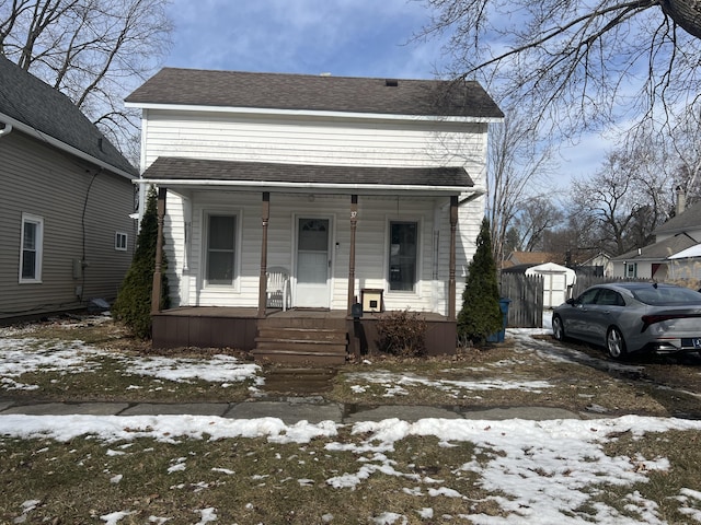 shotgun-style home with a porch and roof with shingles