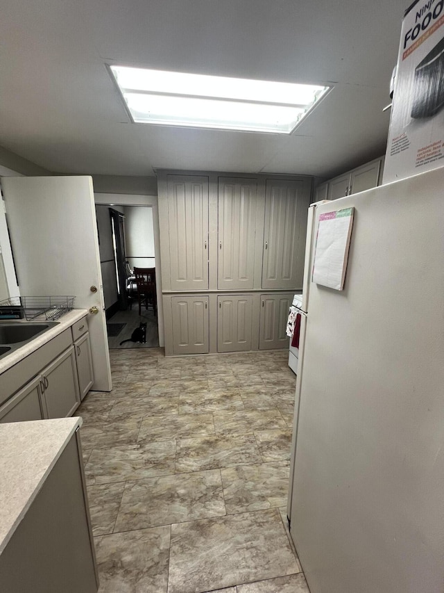 kitchen with gray cabinets, light countertops, white appliances, and a sink