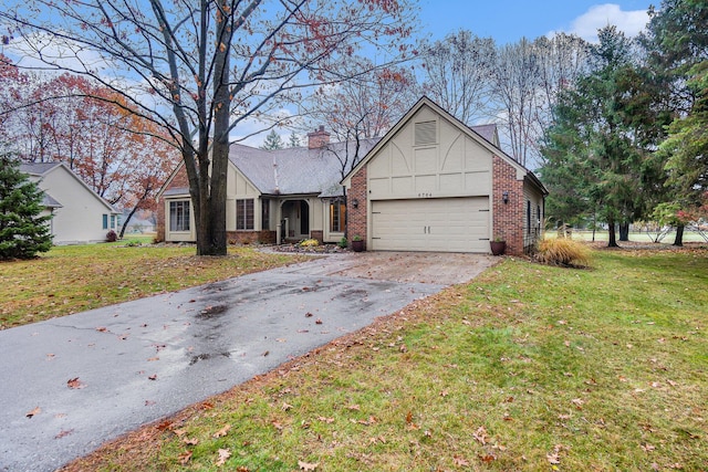 tudor-style house with brick siding, a chimney, a garage, driveway, and a front lawn