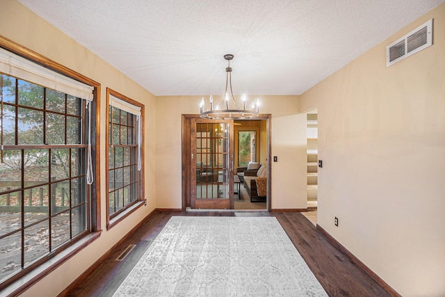 unfurnished dining area featuring dark wood-style floors, a healthy amount of sunlight, visible vents, and a notable chandelier