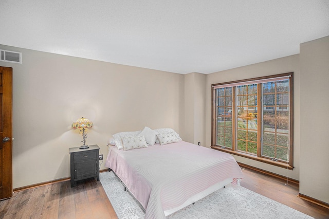 bedroom with baseboards, visible vents, and wood finished floors