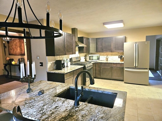 kitchen featuring stainless steel appliances, backsplash, a sink, light stone countertops, and wall chimney exhaust hood