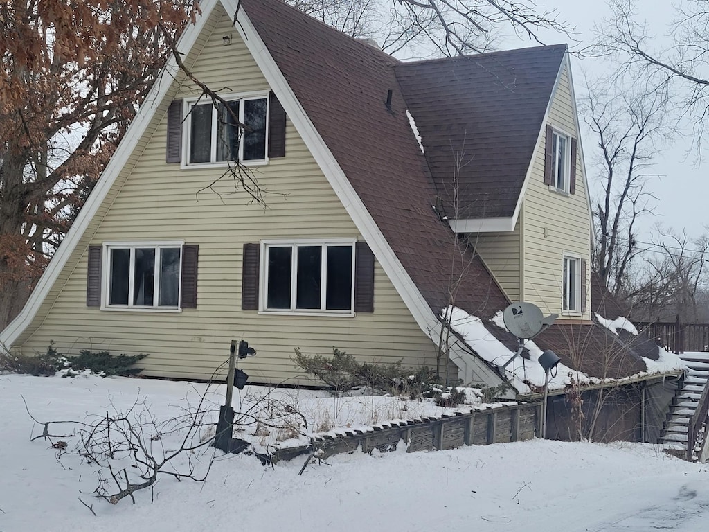 snow covered rear of property featuring roof with shingles