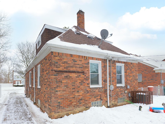 snow covered property featuring brick siding and a chimney