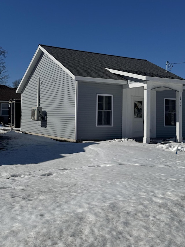 view of snowy exterior featuring a shingled roof and cooling unit