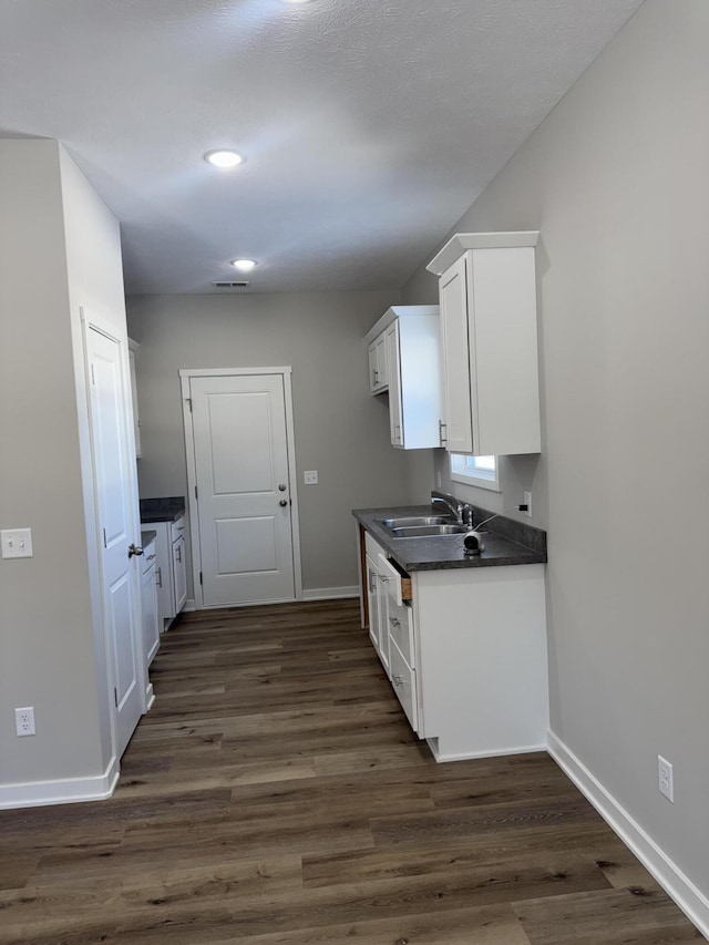 kitchen with dark wood finished floors, dark countertops, white cabinets, a sink, and baseboards