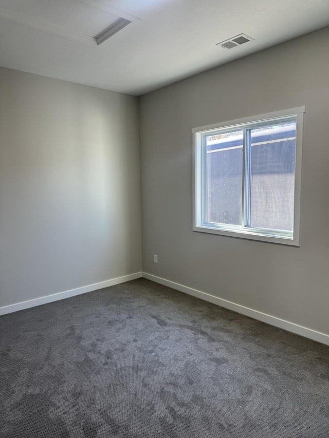 empty room featuring attic access, visible vents, dark carpet, and baseboards