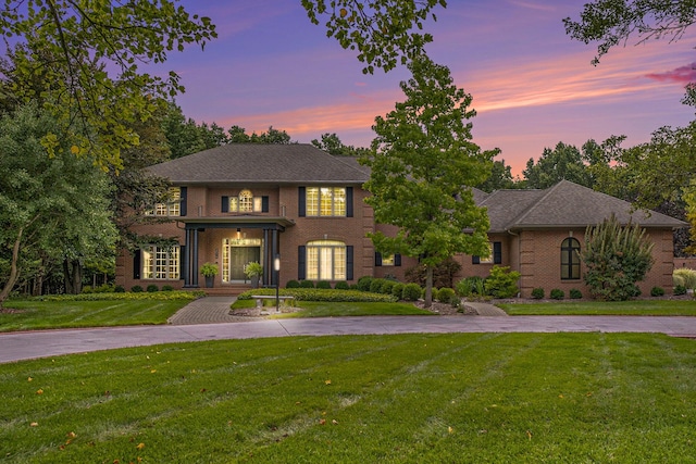 colonial-style house with brick siding, a lawn, and driveway