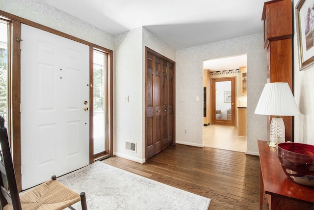 foyer entrance with wallpapered walls, baseboards, visible vents, and dark wood finished floors